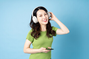 Wall Mural - Asian grasshopper girl portrait is listening to music, isolated on blue background