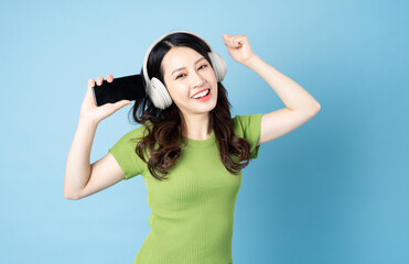 Wall Mural - Asian grasshopper girl portrait is listening to music, isolated on blue background