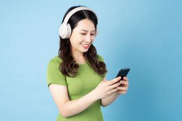 Wall Mural - Asian grasshopper girl portrait is listening to music, isolated on blue background