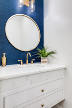 A Small Bathroom With Blue Wallpaper, Gold Hardware, And A White Marble Counter Top.