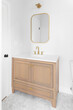 A renovated bathroom with a white marble hexagon floor tile, a natural maple cabinet, and gold faucet, mirror and light.