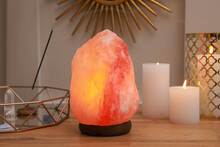 Himalayan Salt Lamp, Candles And Crystals On Wooden Table Near White Wall Indoors