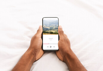 Black Man Holding Smartphone With Music App Interface While Relaxing In Bed