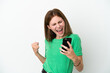 © luismolinero - Young English woman isolated on white background using mobile phone and doing victory gesture