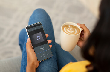 Black Woman Listening Music On Smartphone While Relaxing With Coffee At Home