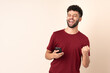 © luismolinero - Young Moroccan man isolated on beige background with phone in victory position