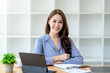 © amnaj - Beautiful young Asian businesswoman sitting looking at camera with laptop in office.