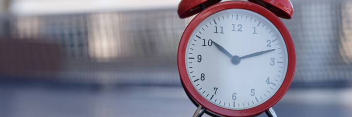 Wall Mural - Red alarm clock standing on tennis table closeup