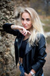 © AlexR - beautiful caucasian blonde female in black leather jacket stands near stone wall in the autumn park