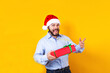 © Marcos - Portrait of young Latin man holding Christmas gift box on a yellow background in Mexico Latin America