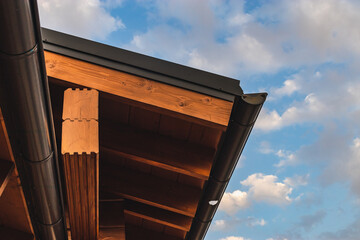 A fragment of the roof of a wooden house in a modern style against a blue cloudy sky. The concept of environmentally friendly housing.