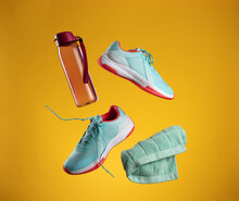 Pink Plastic Water Bottle And Green Towel And Pair Of Textile Blue Sneakers With Laces Levitate On A Yellow Background