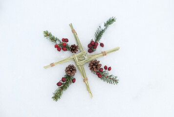 Brigid's cross and fir branches and berries on snow. symbol of Imbolc sabbat. ireland handmade  amulet made from straw. Wiccan tradition for blessed and protected house. flat lay