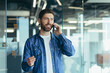 © Liubomir - Smiling young adult bearded hipster professional business man making a business call while talking on the phone in the office, enjoying a corporate mobile conversation indoors, close up