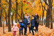 © soleg - Portrait of a family with children in an autumn city park - happy people walking together, they toss the leaves, beautiful nature with yellow leaves as background.