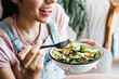 © Marcos - young latin woman eating vegetable or salad bowl, healthy food at home in Mexico Latin America