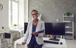© Studio Romantic - Portrait of happy successful satisfied young business lady at work. Beautiful black woman with short hair smiling and looking at camera standing in office interior by table with desktop computers