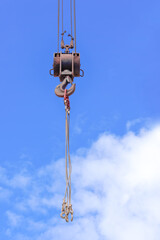 Metal crane hook against the background of the blue sky with the clouds