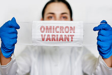 Female Doctor Holds A Face Mask With - Omicron Variant Text On It. Covid-19 New Variant - Omicron. Omicron Variant Of Coronavirus. SARS-CoV-2 Variant Of Concern