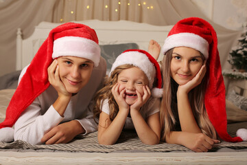 Wall Mural - a young family with a little daughter in Santa Claus hats are lying on the bed at home Christmas