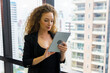 © Patcharanan - Young businesswoman executive using tablet on window with city building background.