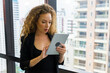 © Patcharanan - Young businesswoman executive using tablet on window with city building background.
