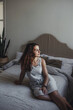 © Tatsiana - A beautiful girl in a dress sits thoughtfully on the bed at home
