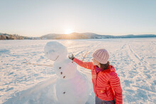 Woman Making Snowman In Winter Lake Snow Nature Landscape Having Fun Enjoying Active Winter Lifestyle At Beautiful Sunset On Sunny Winter Day.