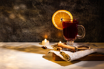 Wall Mural - mulled wine with orange slice on wooden plate with towel on white ang dark background. led light candle 