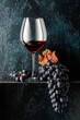 © Igor Normann - Glass of red wine and blue grapes with dried up vine leaves on an old dark blue background.
