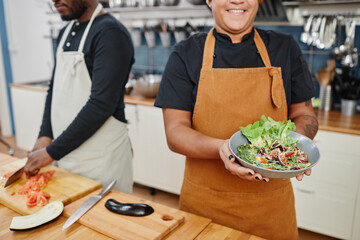 Wall Mural - Cropped shot of female cook holding bowl with vegetable salad while working in professional kitchen, copy space