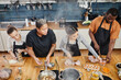 © Seventyfour - High angle portrait of female chef frying meat during cooking class with diverse group of people in kitchen interior