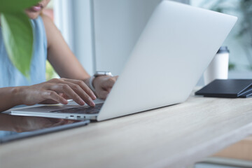 Wall Mural - Closeup of asian business woman in casual wear working on laptop computer, surfing the internet with mobile phone, cup of coffee on table