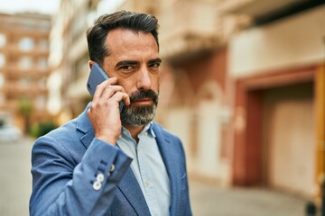 Wall Mural - Middle age businessman with serious expresison talking on the smartphone at the city.