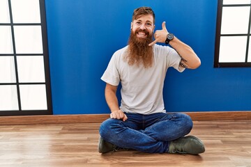 Sticker - Redhead man with long beard sitting on the floor at empty room smiling doing phone gesture with hand and fingers like talking on the telephone. communicating concepts.