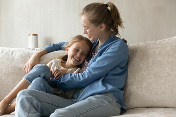 Wall Mural - Caring millennial mother tickling adorable small kid daughter, having fun together resting on couch, enjoying spending weekend leisure time together, showing sincere multigenerational family relations