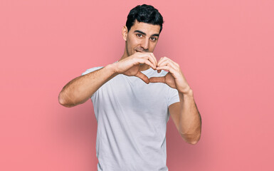 Handsome hispanic man wearing casual white t shirt smiling in love doing heart symbol shape with hands. romantic concept.