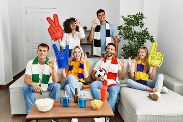 Sticker - Group of friends supporting football team watching tv al home sitting on the sofa doing ok sign with fingers, smiling friendly gesturing excellent symbol