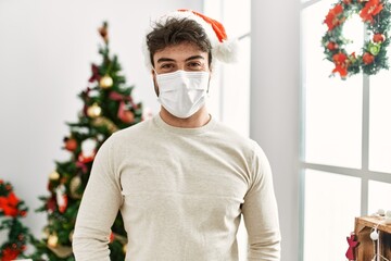 Canvas Print - Young hispanic man smiling happy wearing christmas hat and medical mask at home.