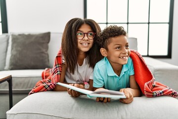 Canvas Print - Two siblings lying on the sofa reading a book looking away to side with smile on face, natural expression. laughing confident.