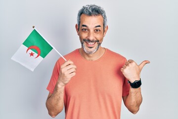 Sticker - Handsome middle age man with grey hair holding algeria flag pointing thumb up to the side smiling happy with open mouth