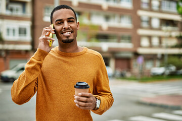 Wall Mural - Young african american man talking on the smartphone drinking coffee at the city.