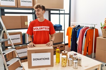 Sticker - Young caucasian man volunteer holding donations box looking away to side with smile on face, natural expression. laughing confident.