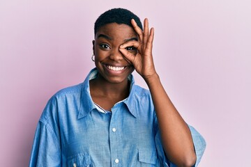 Young african american woman wearing casual clothes doing ok gesture with hand smiling, eye looking through fingers with happy face.