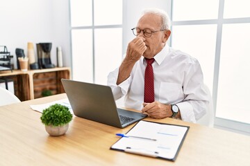 Canvas Print - Senior man working at the office using computer laptop smelling something stinky and disgusting, intolerable smell, holding breath with fingers on nose. bad smell