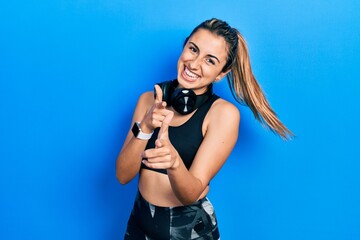 Poster - Beautiful hispanic woman wearing gym clothes and using headphones pointing fingers to camera with happy and funny face. good energy and vibes.