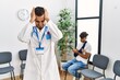 © Krakenimages.com - Hispanic doctor man at waiting room with pacient with arm injury suffering from headache desperate and stressed because pain and migraine. hands on head.