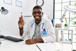 © Krakenimages.com - Young african american doctor man holding electronic cigarette at medical clinic looking positive and happy standing and smiling with a confident smile showing teeth