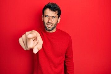 Handsome man with beard wearing casual red sweater pointing displeased and frustrated to the camera, angry and furious with you