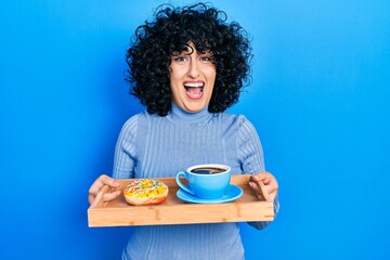 Poster - Young middle east woman holding tray with doughnut and cup of coffee celebrating crazy and amazed for success with open eyes screaming excited.